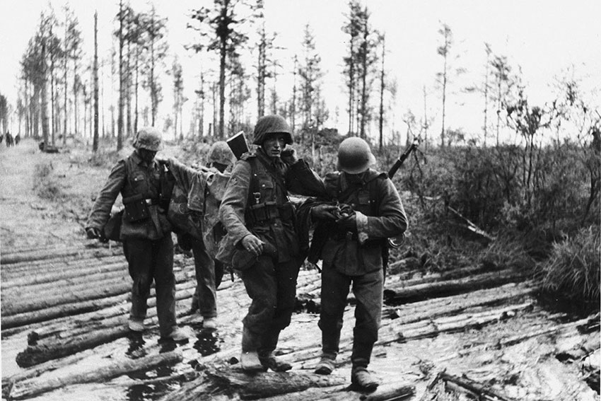 Немецкие солдаты несут раненого на носилках во время боев... Немецкие солдаты несут раненого на носилках во время боев...
